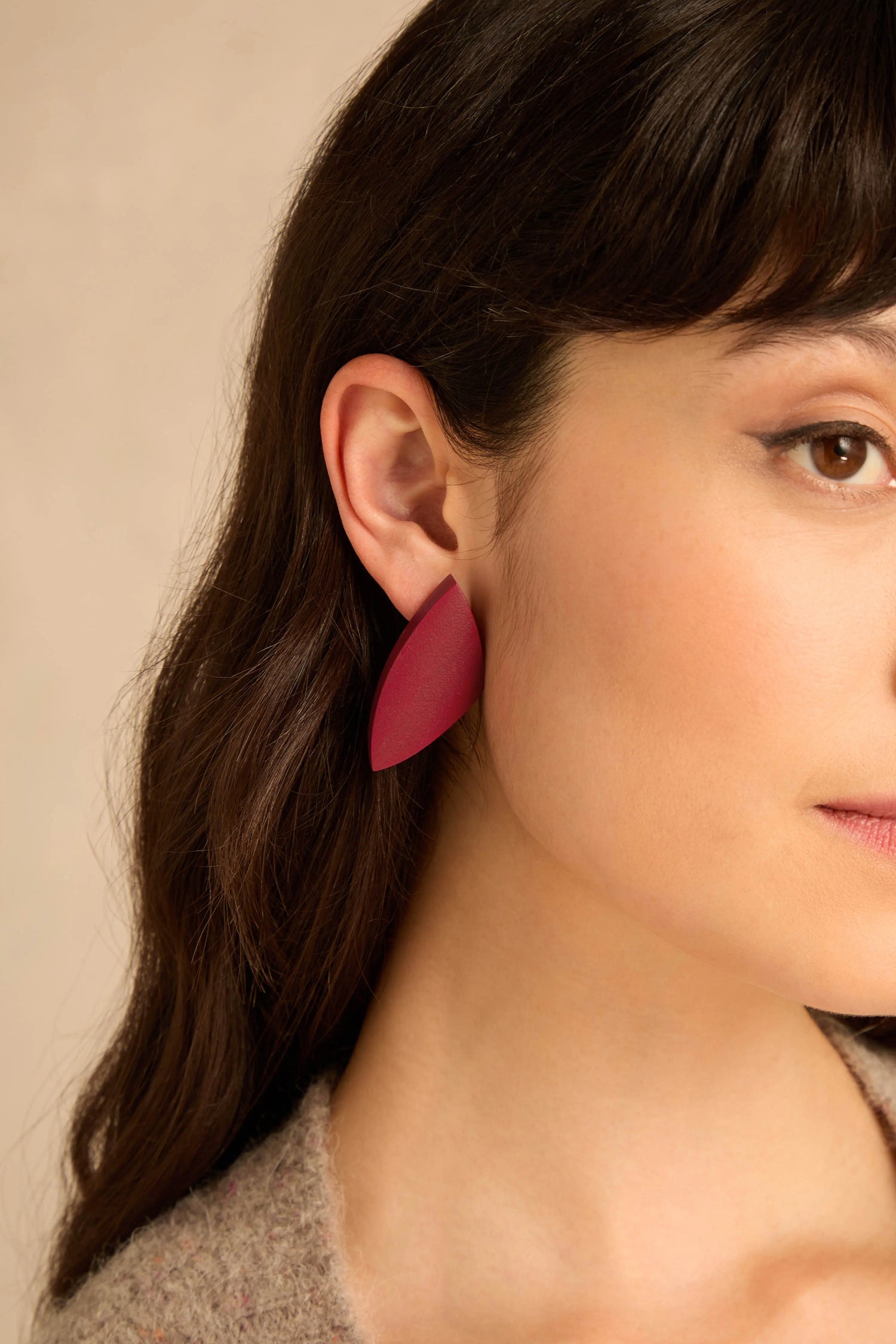 A woman wearing Sculptural Mango Red Wood Earrings featuring a curved, red, leaf-shaped design.