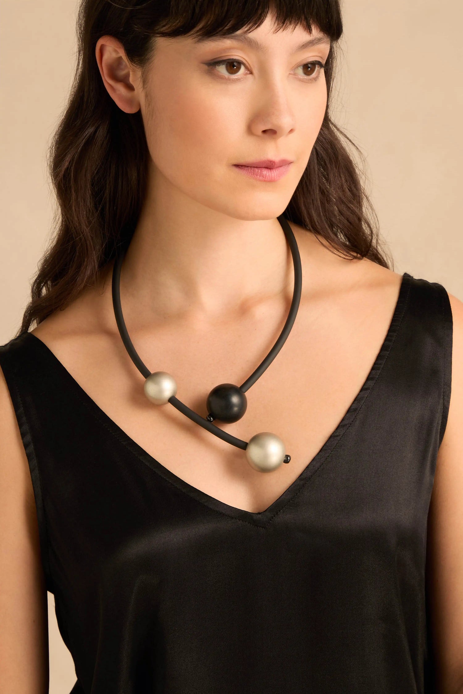 A woman wears a black and silver Triple Sphere Statement Necklace featuring three spherical beads on a black cord.