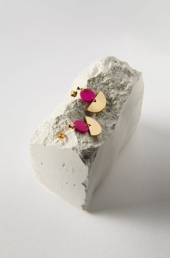 Introducing the Colour Pop Semi Circle Earrings—featuring a minimalist gold and pink teardrop design with semicircular details. Elegantly displayed on a rough white block, these rubberised metal earrings offer a subtle touch of sophistication.
