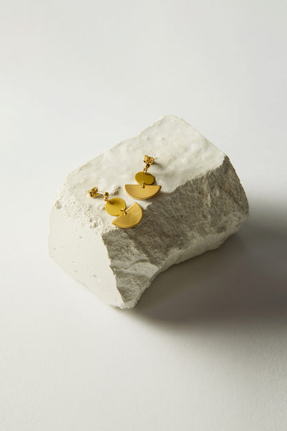 Colour Pop Semi Circle Earrings, crafted with circular and semi-circular designs in gold, elegantly rest on a textured white stone surface. These minimalist earrings add a touch of sophistication to any outfit.