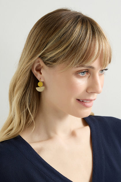 A blonde woman wears minimalist Colour Pop Semi Circle Earrings in gold and a navy V-neck top, gazing sideways against a plain background.
