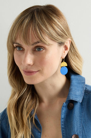 A person with long blonde hair wears a blue button-up shirt and vibrant Colour Pop Circle Drop Earrings in blue and yellow.