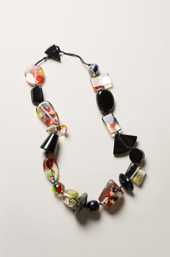 The Short Multi Shapes Resin Necklace showcases handcrafted, colorful resin beads—black, clear, and multicolored—arranged on a black string and displayed against a light background.