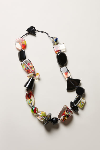The Short Multi Shapes Resin Necklace showcases handcrafted, colorful resin beads—black, clear, and multicolored—arranged on a black string and displayed against a light background.