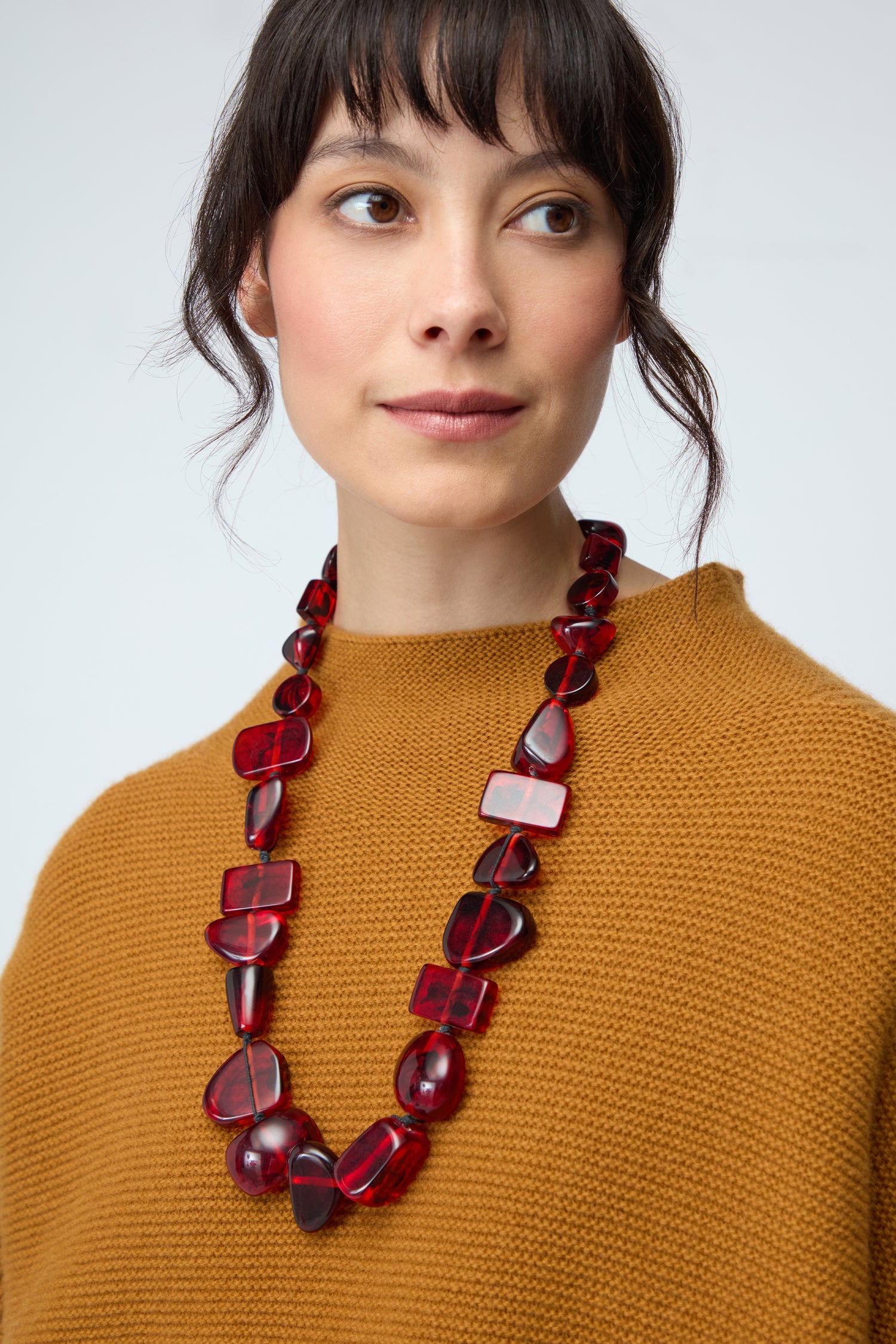 A woman wearing a mustard brown knit top and the Ruby Resin Bead Necklace gazes slightly to the right against a plain background.