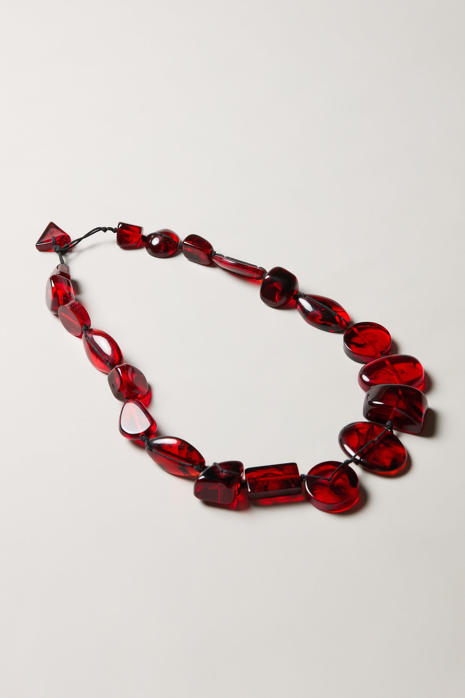The Ruby Resin Bead Necklace features handmade, irregularly shaped translucent red resin beads, beautifully displayed on a plain white surface.