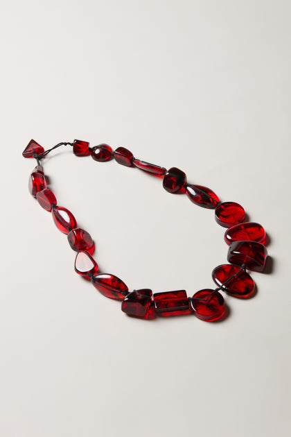 The Ruby Resin Bead Necklace features handmade, irregularly shaped translucent red resin beads, beautifully displayed on a plain white surface.