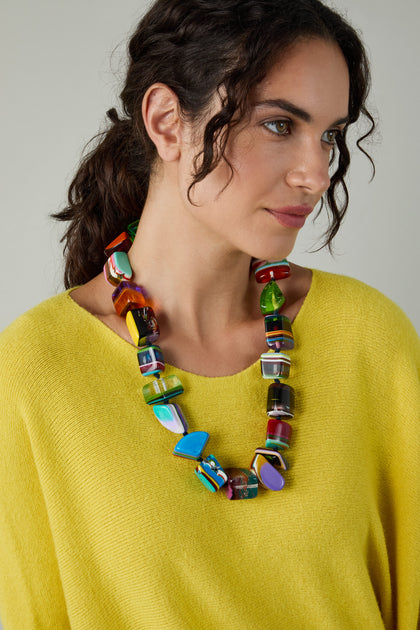 Woman wearing a yellow sweater and the Kandinsky Pop Art Pebble Necklace—a chunky, multicolored abstract statement piece—looks to the side against a neutral background.