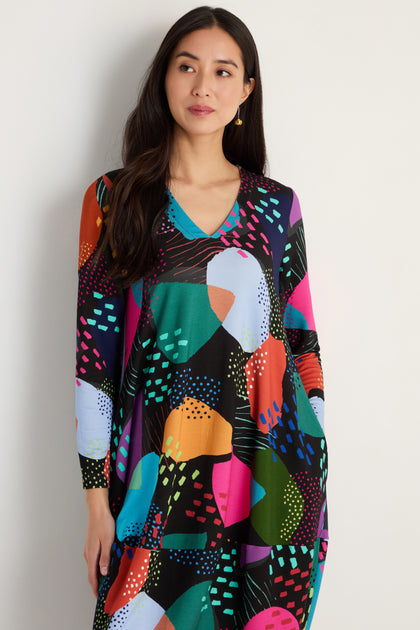 A woman in the Mark Making Print Jersey Bubble Dress, featuring a colorful printed pattern and made in England.