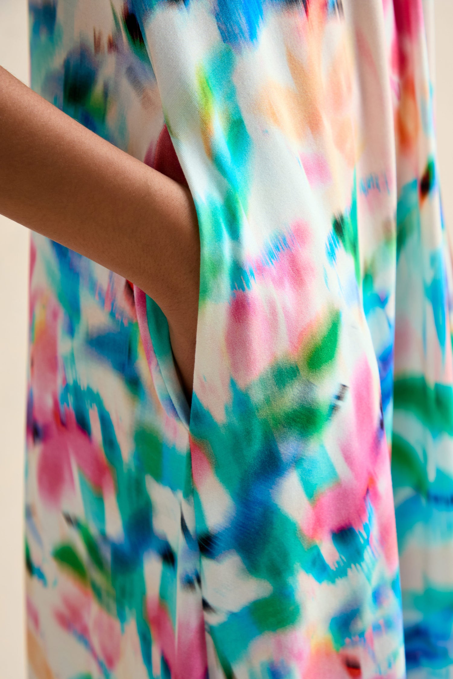 A person’s hand is placed in the pocket of a Petal Haze Jersey Flare Dress, which features a colorful, abstract, watercolor-like pattern.