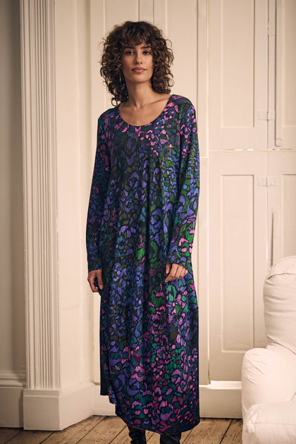 A woman wearing a Winter Garden Jersey Bubble Dress with long sleeves, a scoop neck, and an abstract multicolored pattern of blue, purple, and green.
