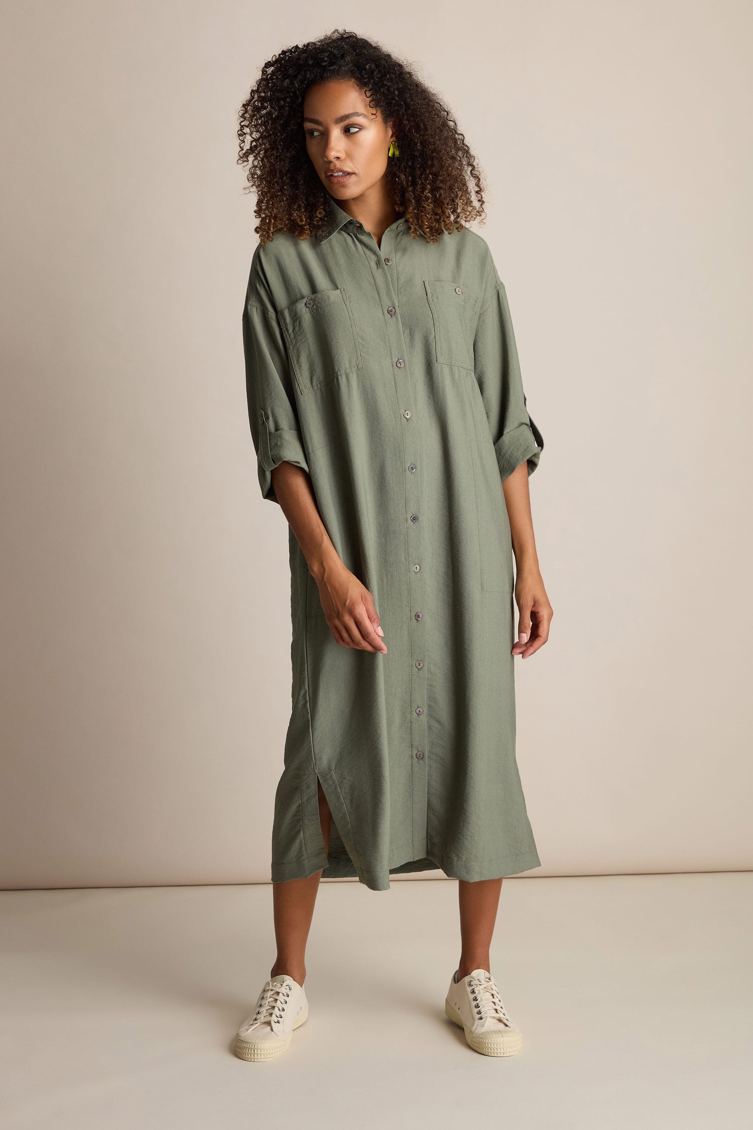 A person wearing a long Textured Viscose Shirt Dress in a khaki colorway and white sneakers stands against a plain background.