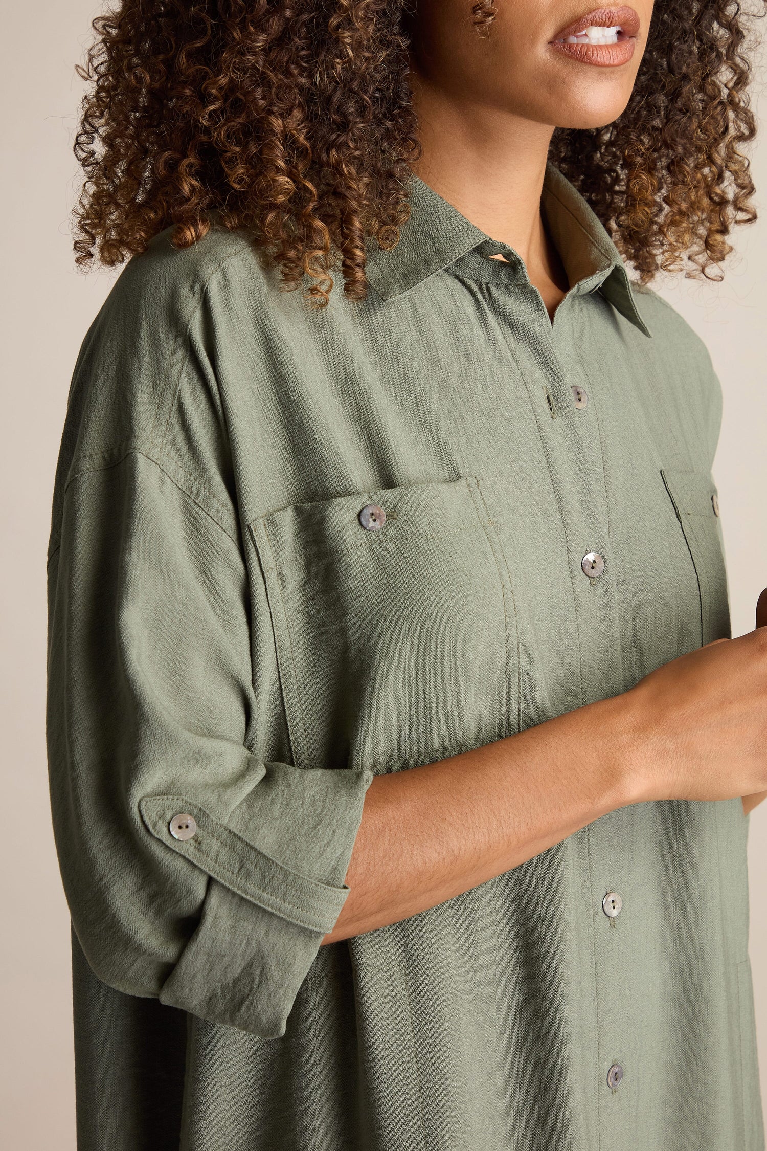 A person with curly hair is wearing a buttoned-up, long-sleeve, green Textured Viscose Shirt Dress with buttoned pockets. Their face is partially visible.