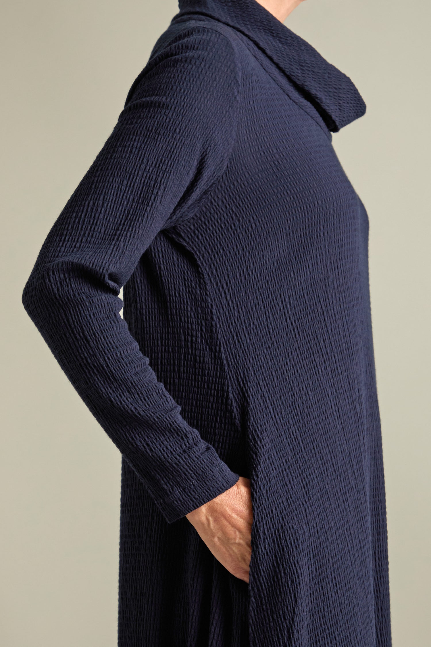 Person wearing a textured, long-sleeved Crinkle Viscose Bubble Dress in navy blue, with their right hand in a side pocket, depicted from the shoulders down against a neutral background, presenting a relaxed chic and voluminous silhouette.