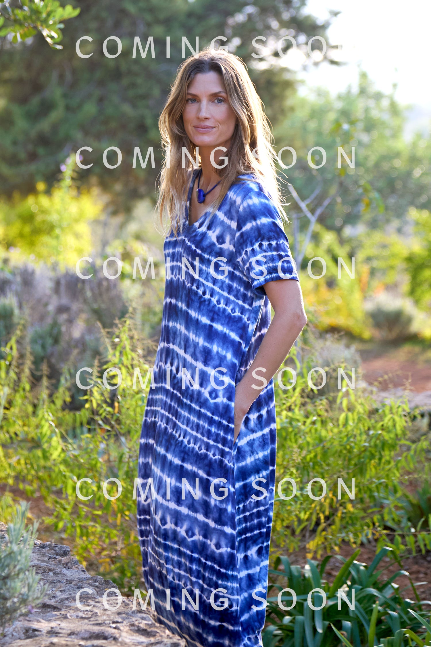 Person outdoors in the Tie Dye Jersey Bubble Dress (code JFD6336-TDP) stands amid lush greenery with "COMING SOON" gracefully overlaid, creating a tranquil natural backdrop.