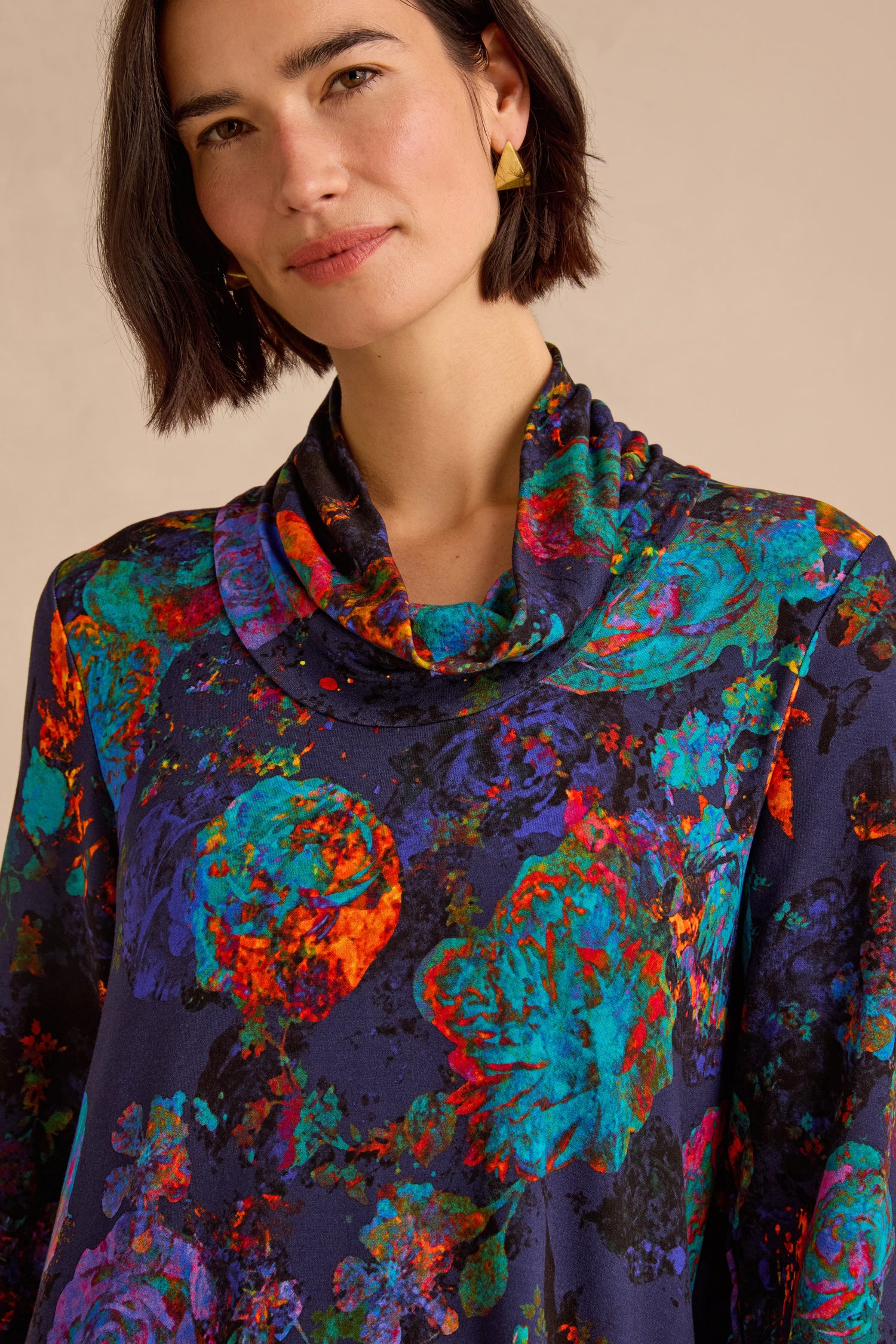 A woman with short dark hair poses against a neutral background wearing the Midnight Floral Jersey Bubble Dress— a colorful, floral-patterned, cowl-neck midi dress featuring a soft bubble silhouette.