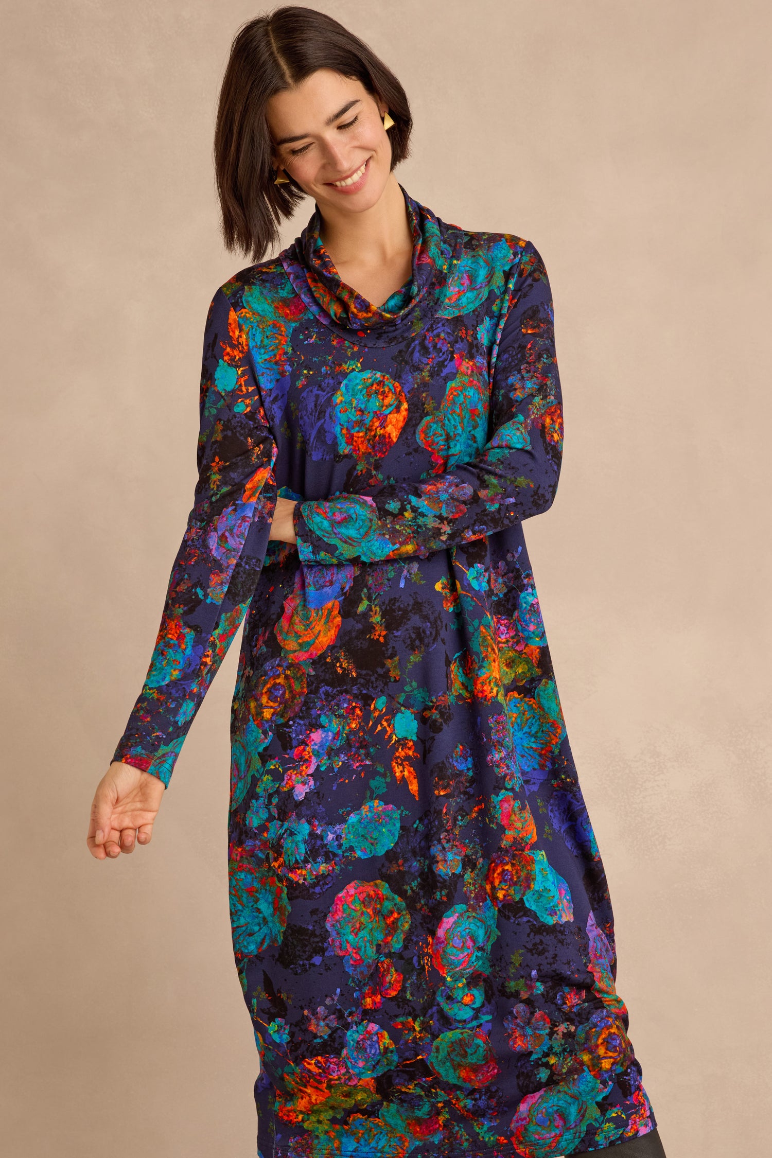 A woman stands against a neutral background, smiling with her eyes closed, wearing the Midnight Floral Jersey Bubble Dress—a long-sleeve, midi-length dress featuring a colorful abstract pattern and a subtle bubble silhouette.
