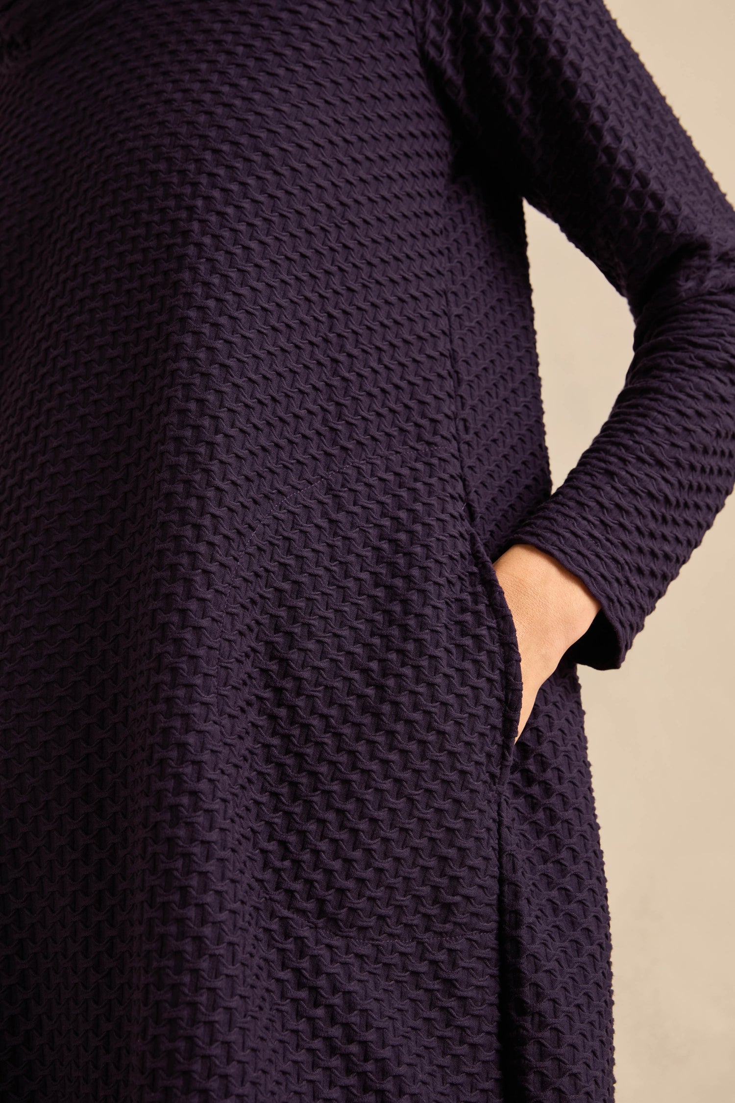 Close-up of a person wearing the Damson Waffle Textured Jersey Bubble Dress, with one hand tucked into a side pocket.
