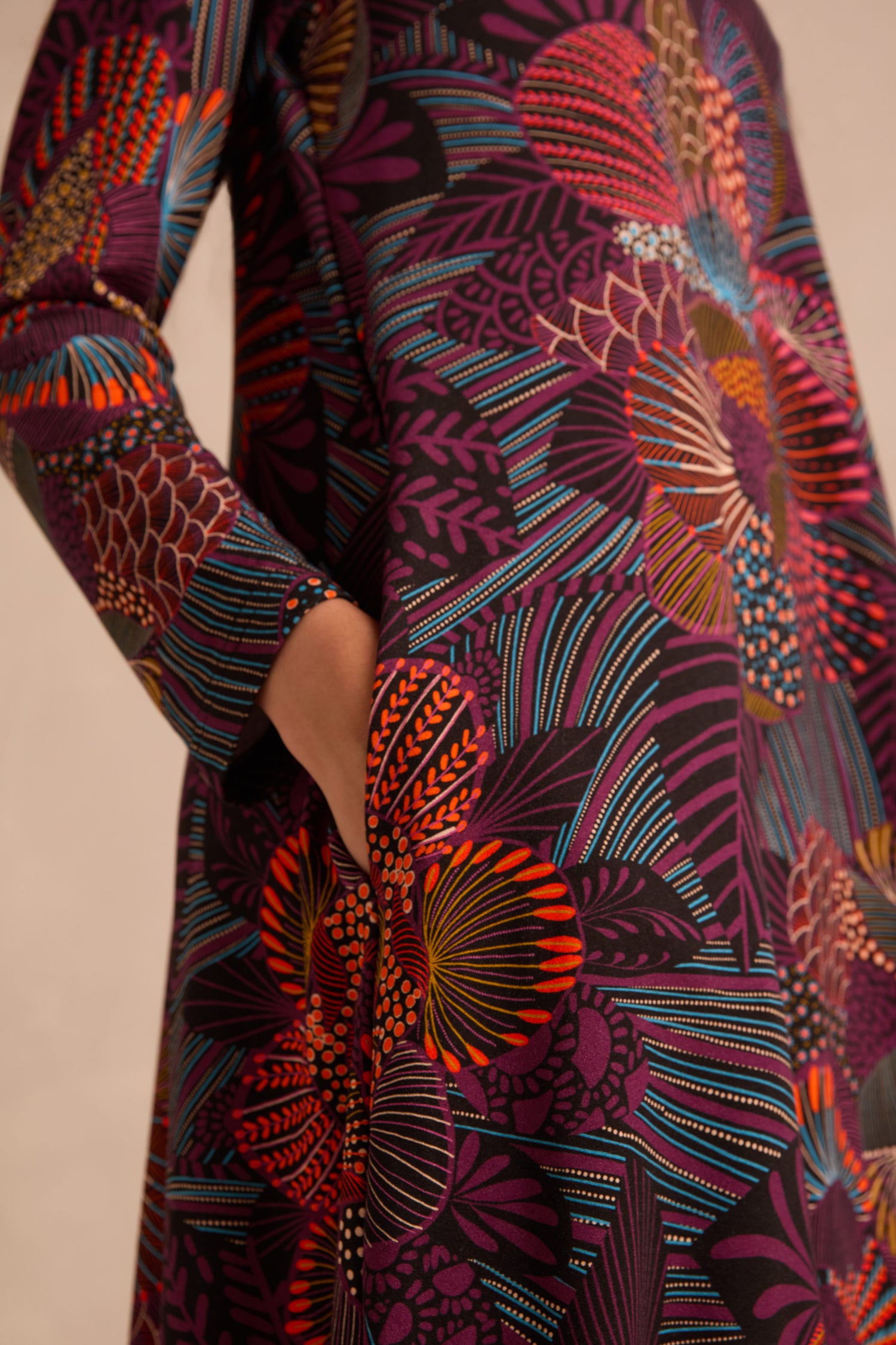 A person wears the Abstract Linear Floral Jersey Bubble Dress, featuring long sleeves and a colorful geometric floral pattern in shades of purple, orange, red, and blue, with one hand tucked into a pocket.