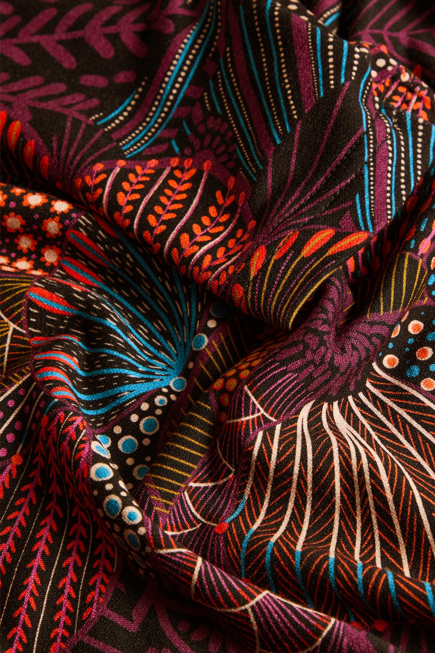 The Abstract Linear Floral Jersey Bubble Dress showcases colorful fabric adorned with intricate botanical and geometric motifs in red, blue, orange, and white on a black background. Displayed with visible folds, this dress is perfect for making a bold statement with its vibrant linear floral patterns.