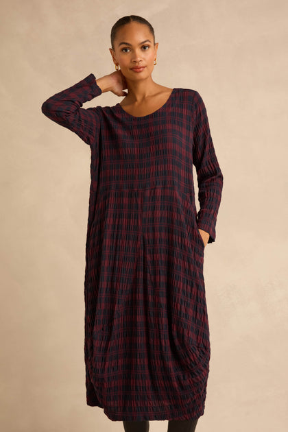 A person wearing a Crinkle Check Bubble Dress, featuring a midi length, long-sleeved silhouette in a dark red and black plaid pattern.