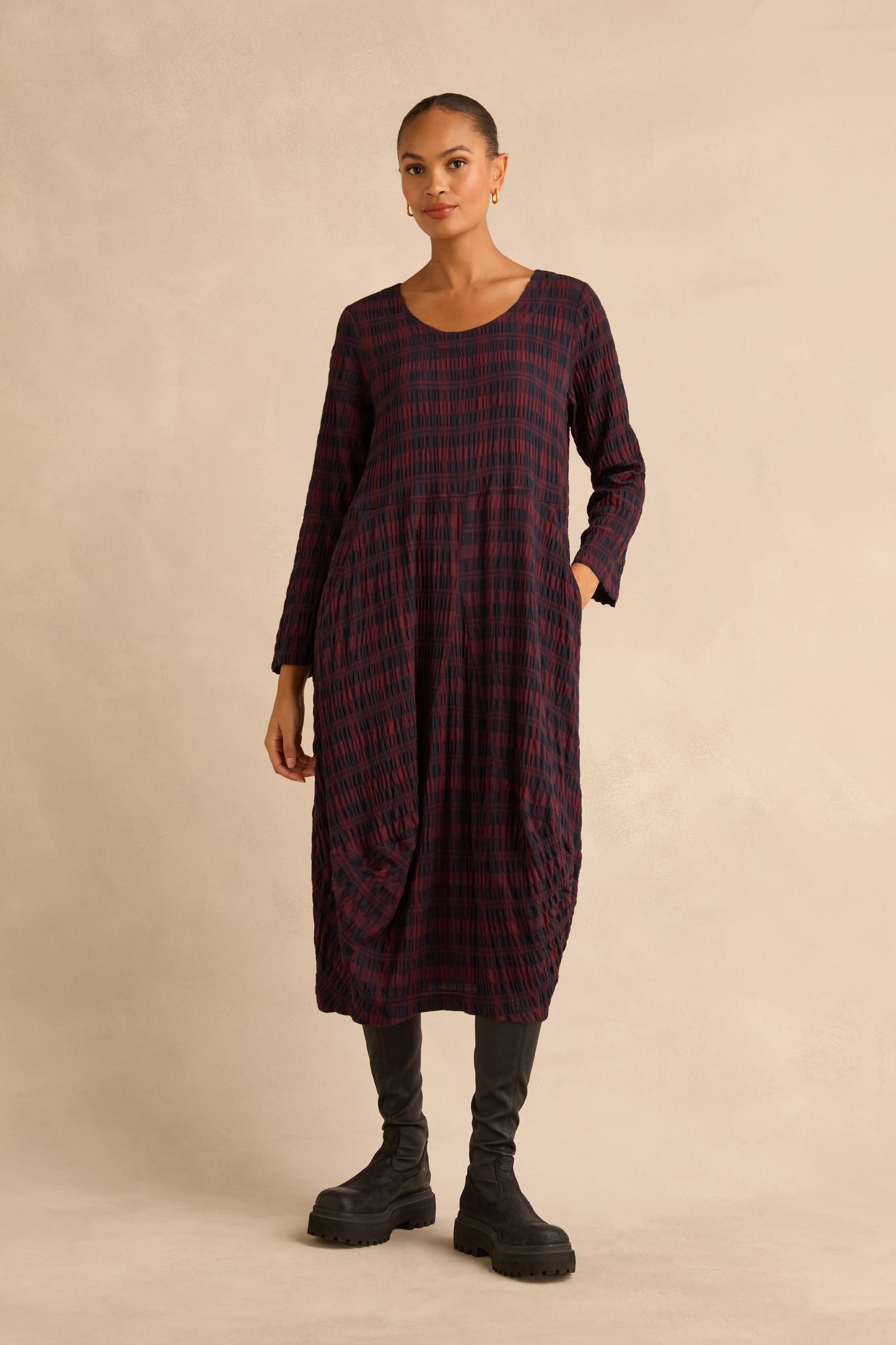 A person wearing a midi-length Crinkle Check Bubble Dress in a dark red and blue plaid pattern, paired with black boots.