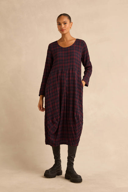 A person wearing a midi-length Crinkle Check Bubble Dress in a dark red and blue plaid pattern, paired with black boots.