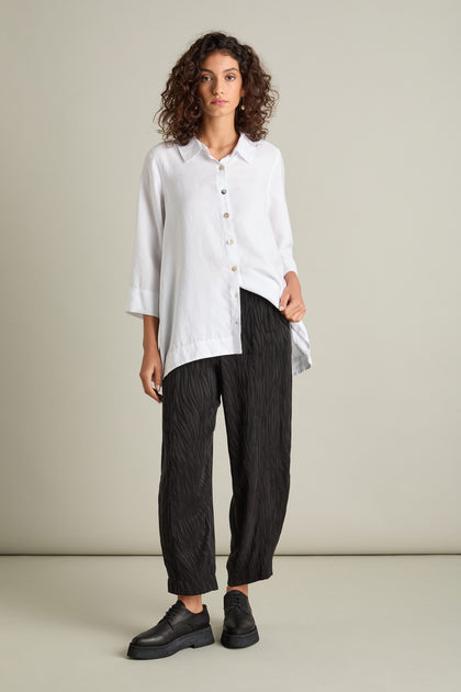 A person with curly hair models a white button-up shirt and the Abstract Lines Jacquard Bubble Trouser, paired with black shoes against a plain background for a contemporary look.