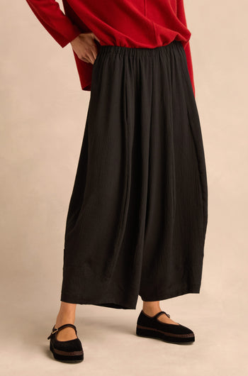 Person wearing a red long-sleeve top, Fine Crinkle Barrel Trousers in black with a cropped length, and black Mary Jane shoes, standing against a neutral background.