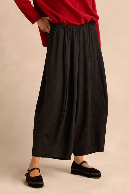 Person wearing a red long-sleeve top, Fine Crinkle Barrel Trousers in black with a cropped length, and black Mary Jane shoes, standing against a neutral background.
