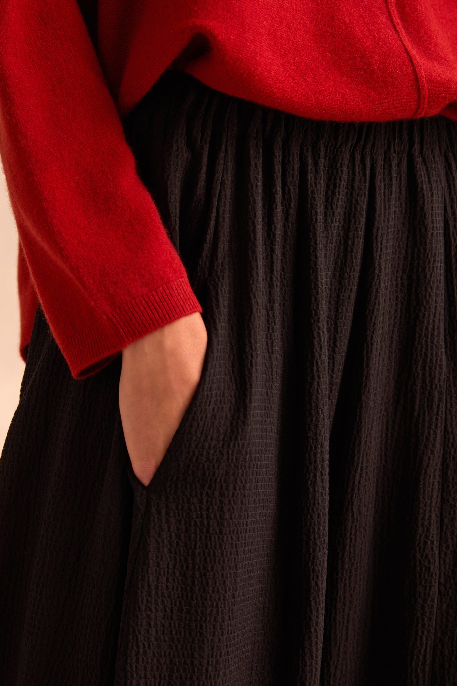 A person wearing a red long-sleeve top and Fine Crinkle Barrel Trousers in black, with one hand in the trouser pocket, showcasing a subtle barrel silhouette for added volume.