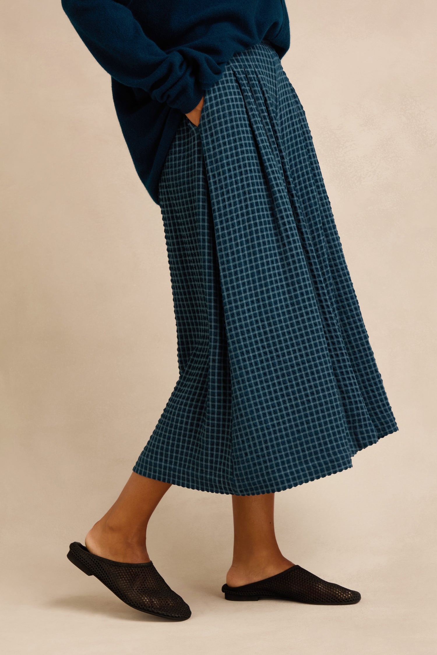 Wearing the Seersucker Squares Wide Trousers in dark blue, paired with a matching top and black slip-on shoes, this look features a person standing with one foot slightly forward against a neutral background—a versatile everyday style that transitions effortlessly from skirt-like elegance to smart pull-on trousers.