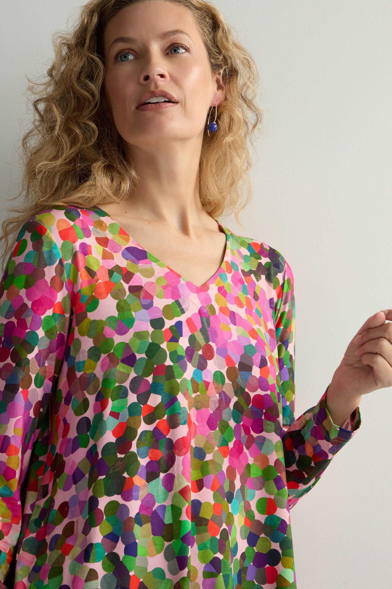 Against a plain background, a person with curly hair wears the Abstract Confetti Jersey Top, showcasing its vibrant design, fit-and-flare silhouette, and V-neck.