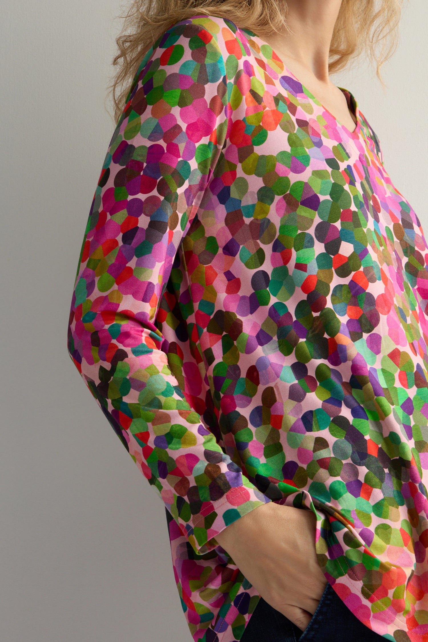 A person in a V-neck Abstract Confetti Jersey Top with a colorful pattern has their hand in their pocket.