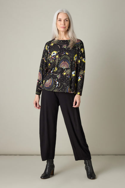 A woman with long gray hair is wearing the Celestial Dreams Jersey Boxy Top and black pants as she stands against a plain background.