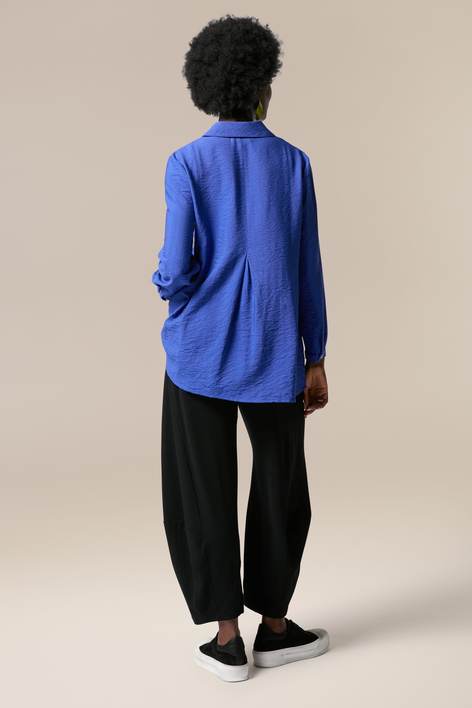 The back view of a woman wearing a Textured Viscose Pleat Shirt and black pants.