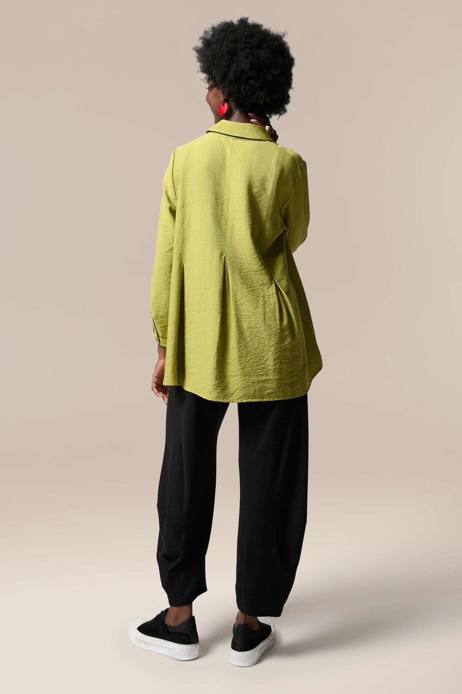 The back view of a woman wearing a Textured Viscose Pleat Shirt and black pants.
