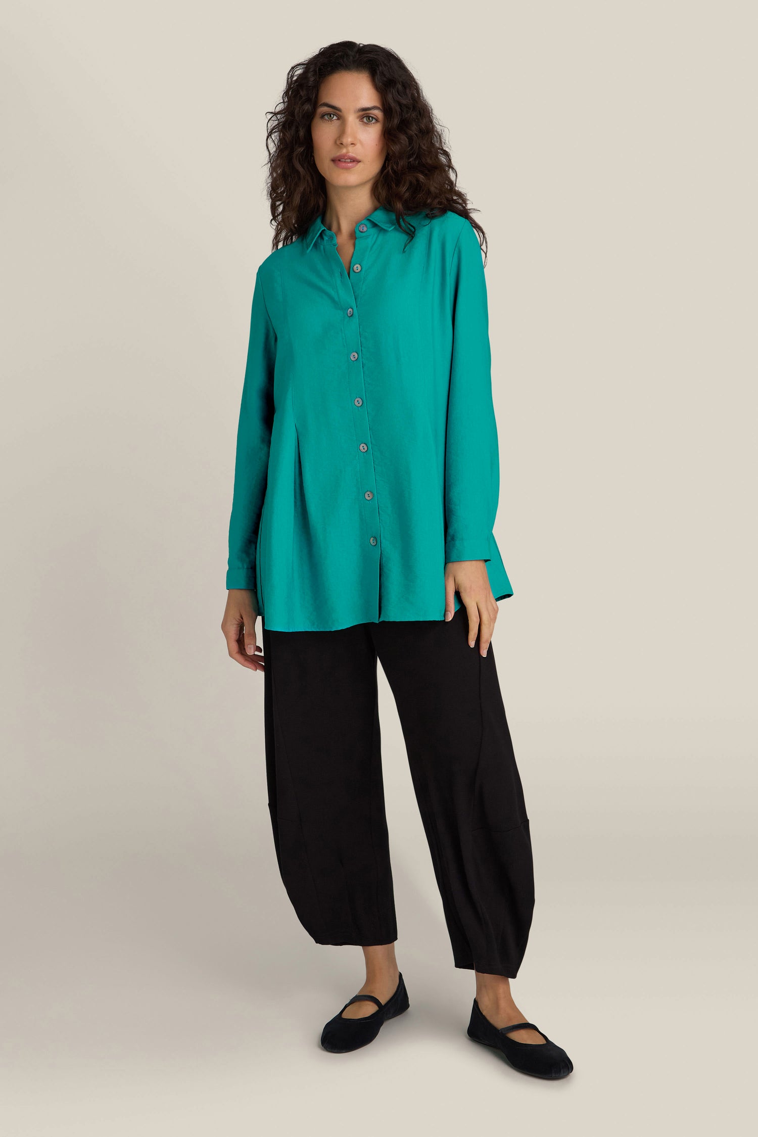 A woman stands against a plain background wearing an elegant, contemporary Textured Viscose Pleat Shirt in stunning turquoise blue and black pants.