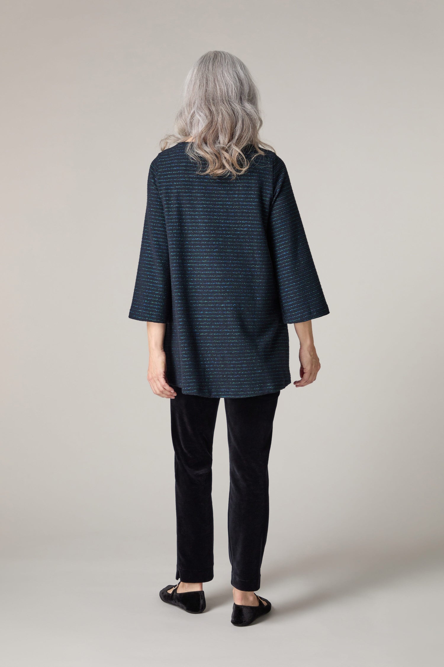 The back view of an older woman wearing a blue jacket and black pants with a hint of sparkle while donning the Stripe Lurex Jersey Top.