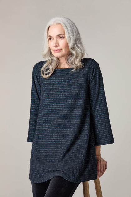 A woman is sitting on a stool wearing a black striped Stripe Lurex Jersey Top, adding a subtle statement with a touch of sparkle.