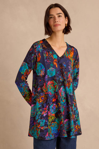 A woman wearing the Midnight Floral Jersey Tunic—a long-sleeved, V-neck fit-and-flare top in soft viscose jersey with an abstract floral pattern—stands against a beige background.
