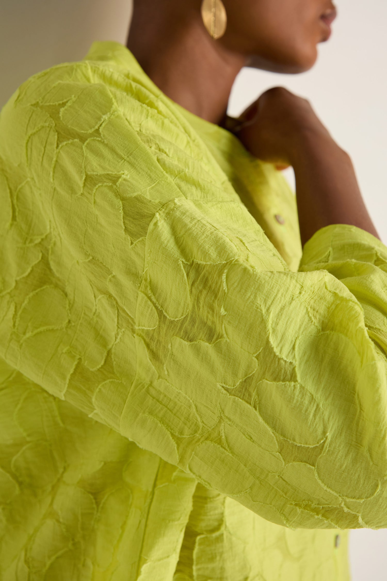 A person in an oversized fit Etched Floral Viscose Shirt—bright yellow-green and textured—with gold earrings, shown from the shoulders up in profile.