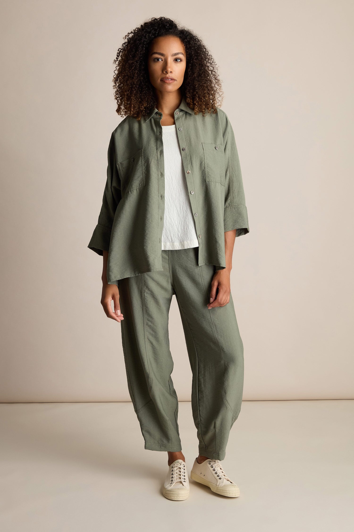 A person with curly hair stands against a plain background, wearing an olive green Textured Viscose Boxy Shirt paired with matching Textured Viscose Bubble Trousers and white sneakers.