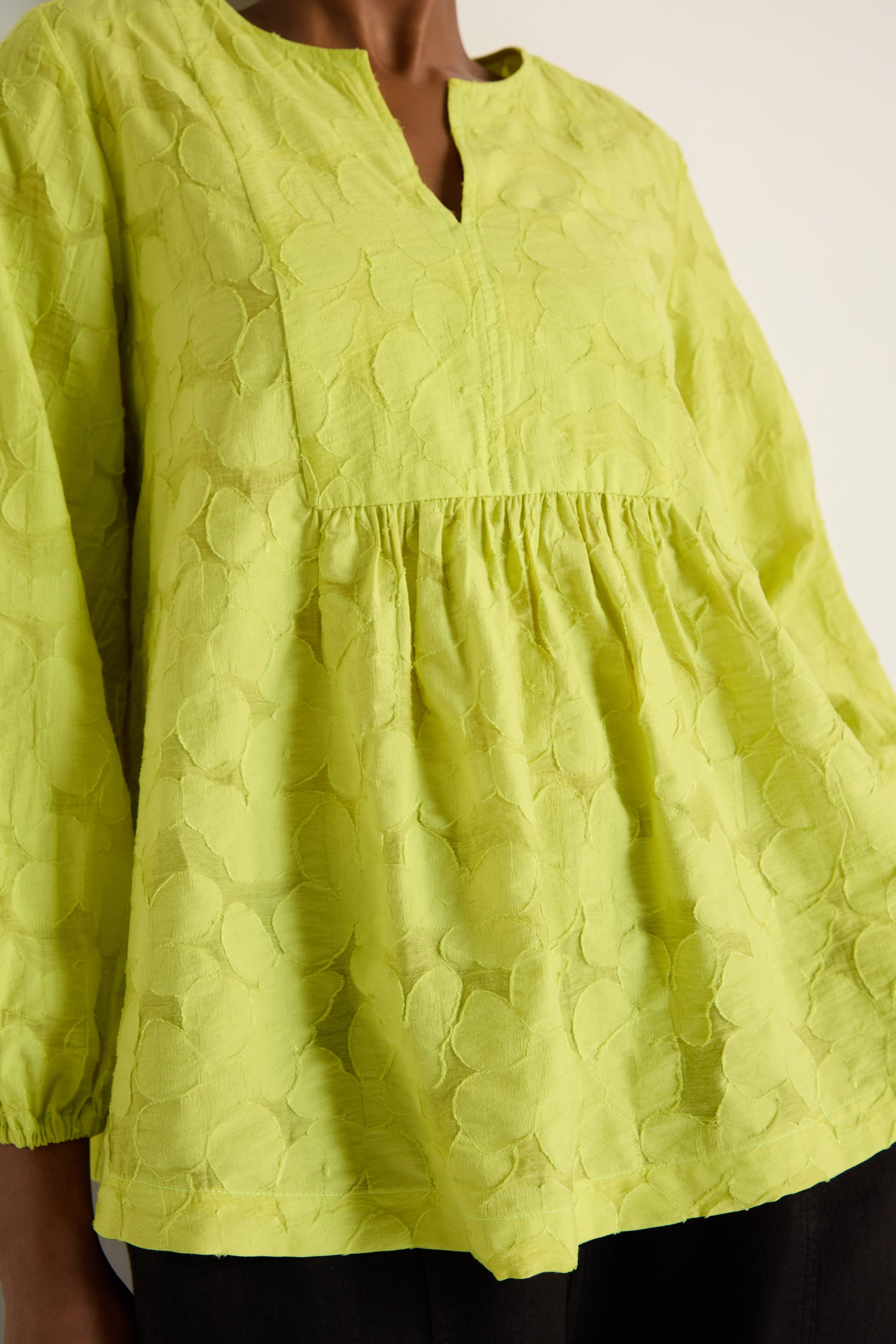 A person wearing the Etched Floral Viscose Top—a loose-fitting, woven floral yellow blouse with a V-neckline and gathered waist detail.