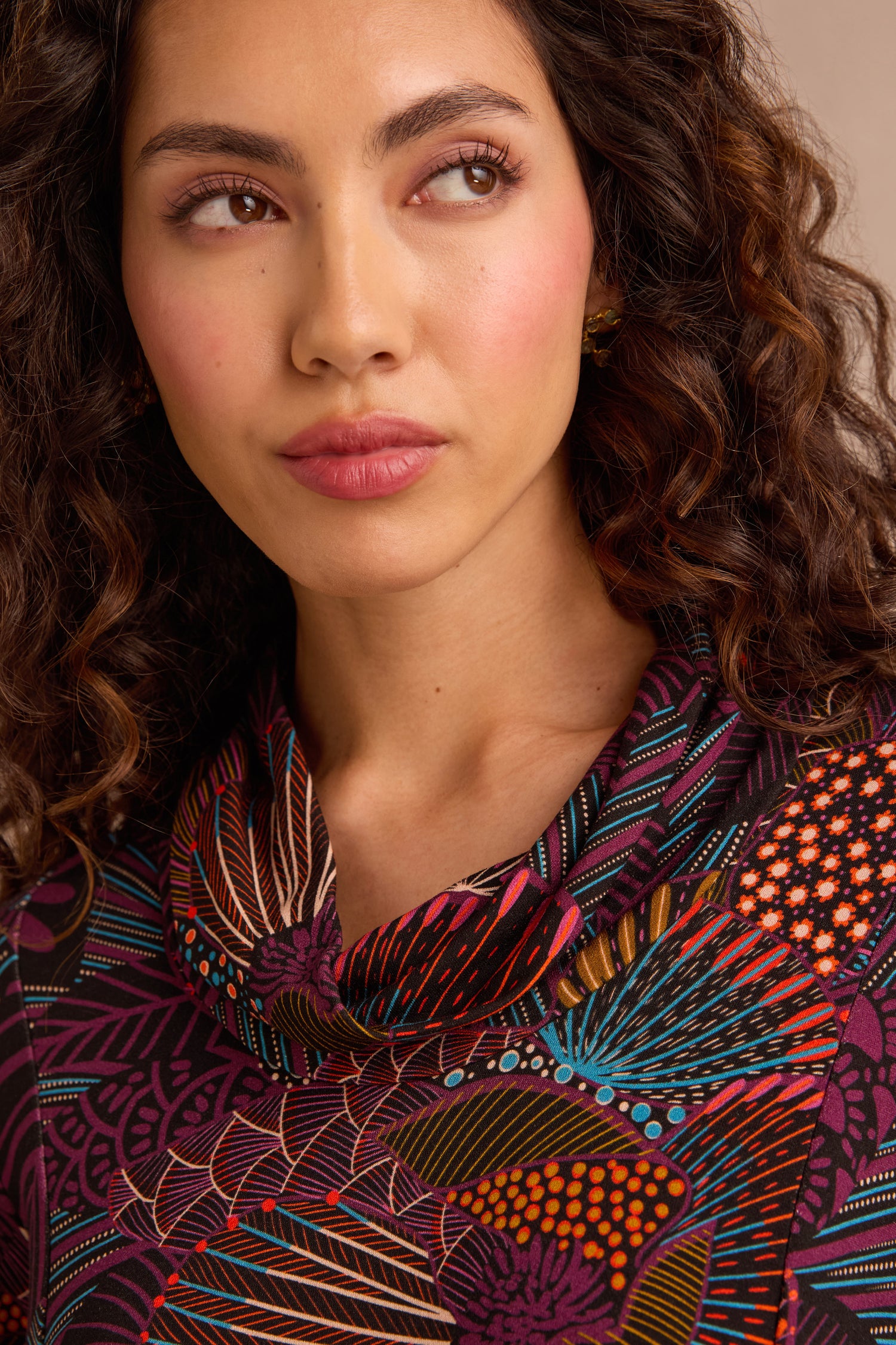 Woman with curly hair wearing the Abstract Linear Floral Jersey Tunic, which features a fit and flare silhouette and a patterned, multicolored design, looks slightly to the side with a neutral expression.