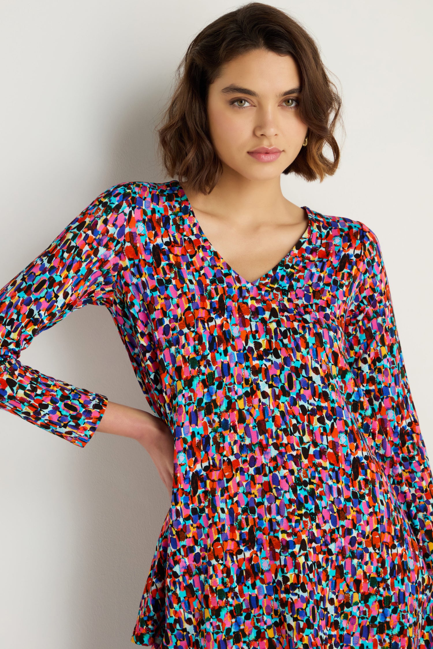 Woman wearing the Painted Spots Jersey Tunic, a long-sleeve viscose jersey top with a multicolored abstract pattern, standing against a plain light background with one hand on her hip.