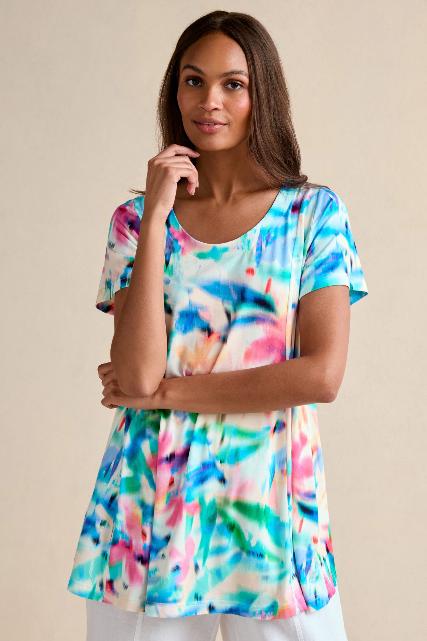 A woman wears the Petal Haze Jersey Tunic, featuring a short-sleeved, relaxed fit and a vibrant abstract print, standing against a plain beige background.