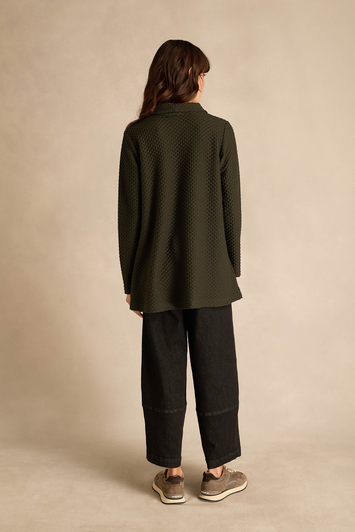 Person standing facing away, wearing a Waffle Textured Jersey Pine Cowl Neck Top, wide black pants, and beige sneakers against a neutral background.