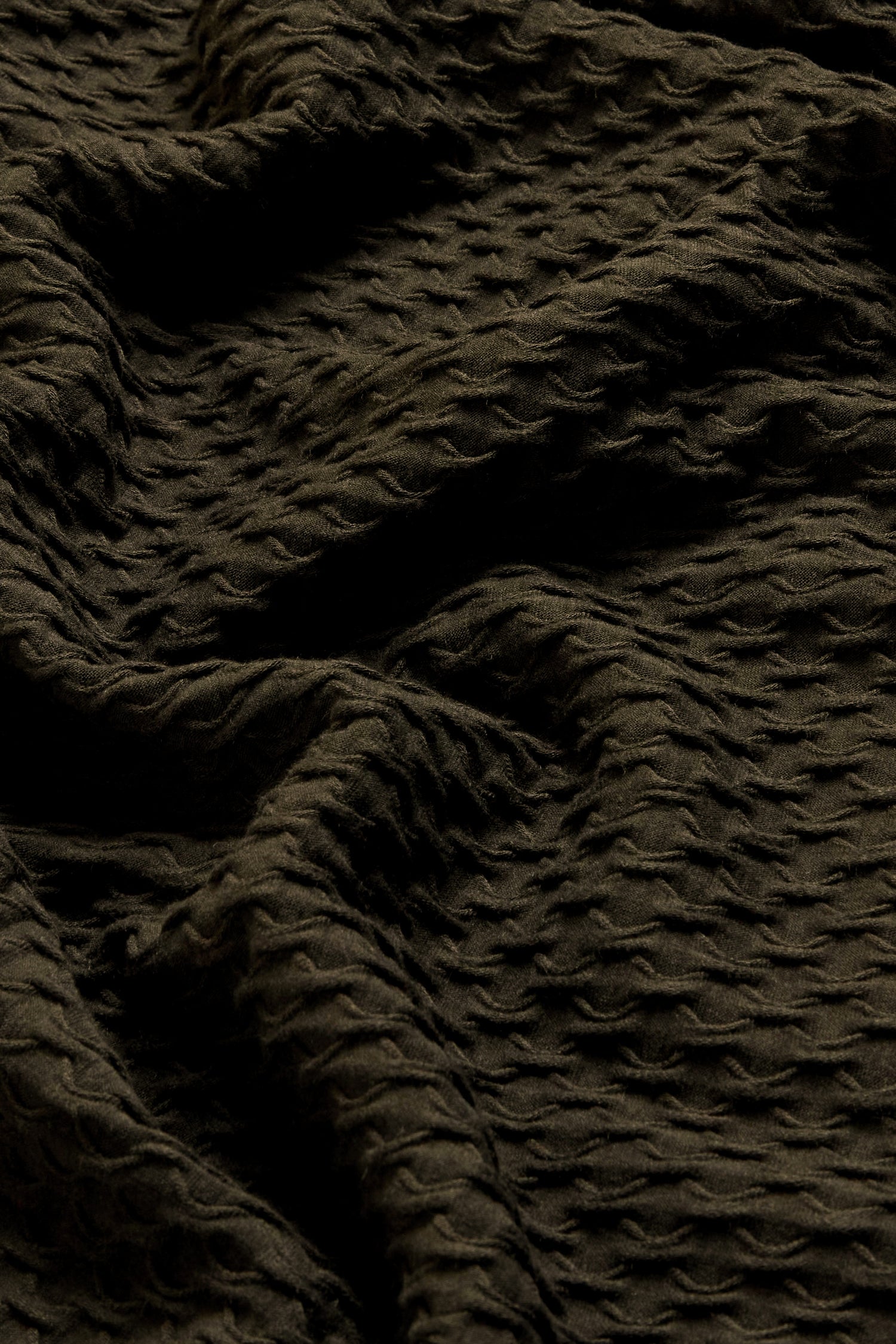 Close-up of the Waffle Textured Jersey Pine Cowl Neck Top, showcasing its dark, textured fabric with a wavy, crinkled pattern and raised dot-like details—folds and shadows highlight the unique waffle texture typical of this English-made design.