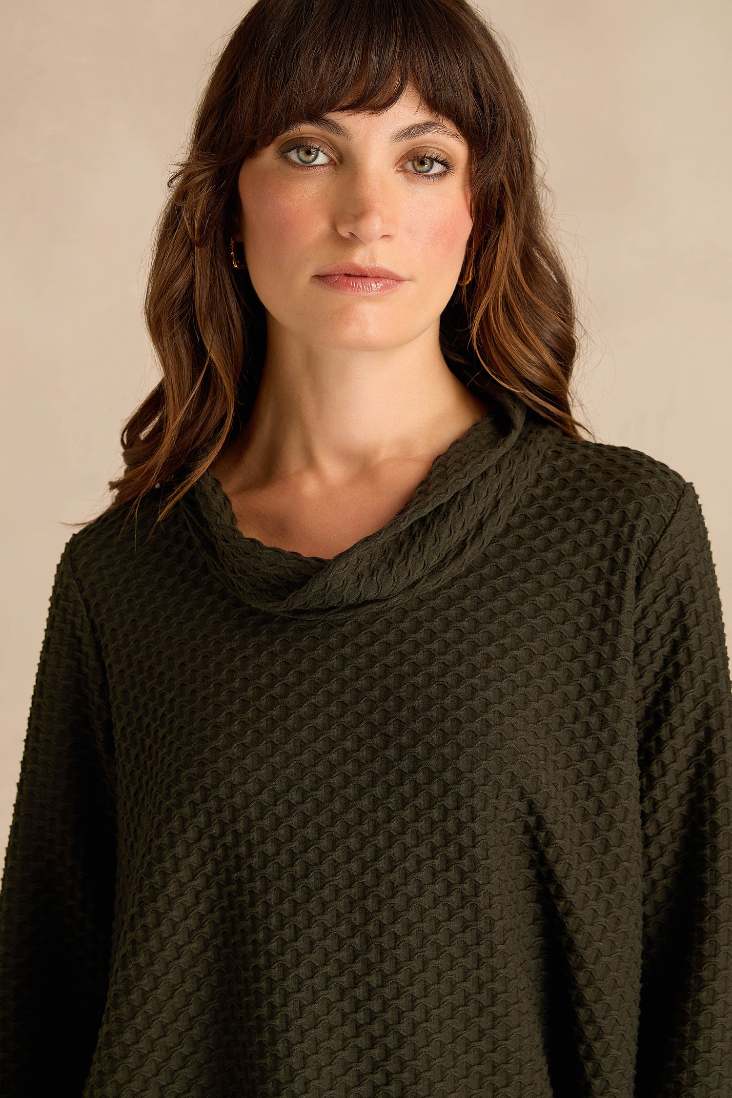 A woman with medium-length brown hair wearing the Waffle Textured Jersey Pine Cowl Neck Top, standing against a plain beige background.